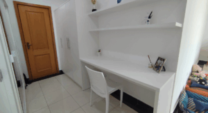 Escrivaninha moderna em quarto com bancada branca, prateleiras flutuantes, cadeira branca e design funcional e minimalista; Creare Ambientes.