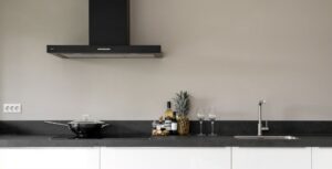 Cozinha contemporânea com bancada preta, armários brancos, coifa preta suspensa, wok preto, torneira em aço inoxidável em design moderno e minimalista. Decoração com abacaxi, taças de vinho e bebidas; Creare Ambientes.