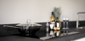 Cozinha moderna com bancada preta, wok preto com tampa de vidro e utensílios de cozinha em ambiente produzido pela Creare Ambientes, especialista em design e decoração.