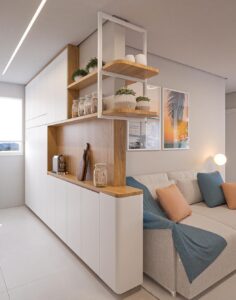 Módulo divisor moderno com armários brancos, bancada de madeira e prateleiras abertas, separando a sala de estar de uma cozinha integrada em um ambiente minimalista.